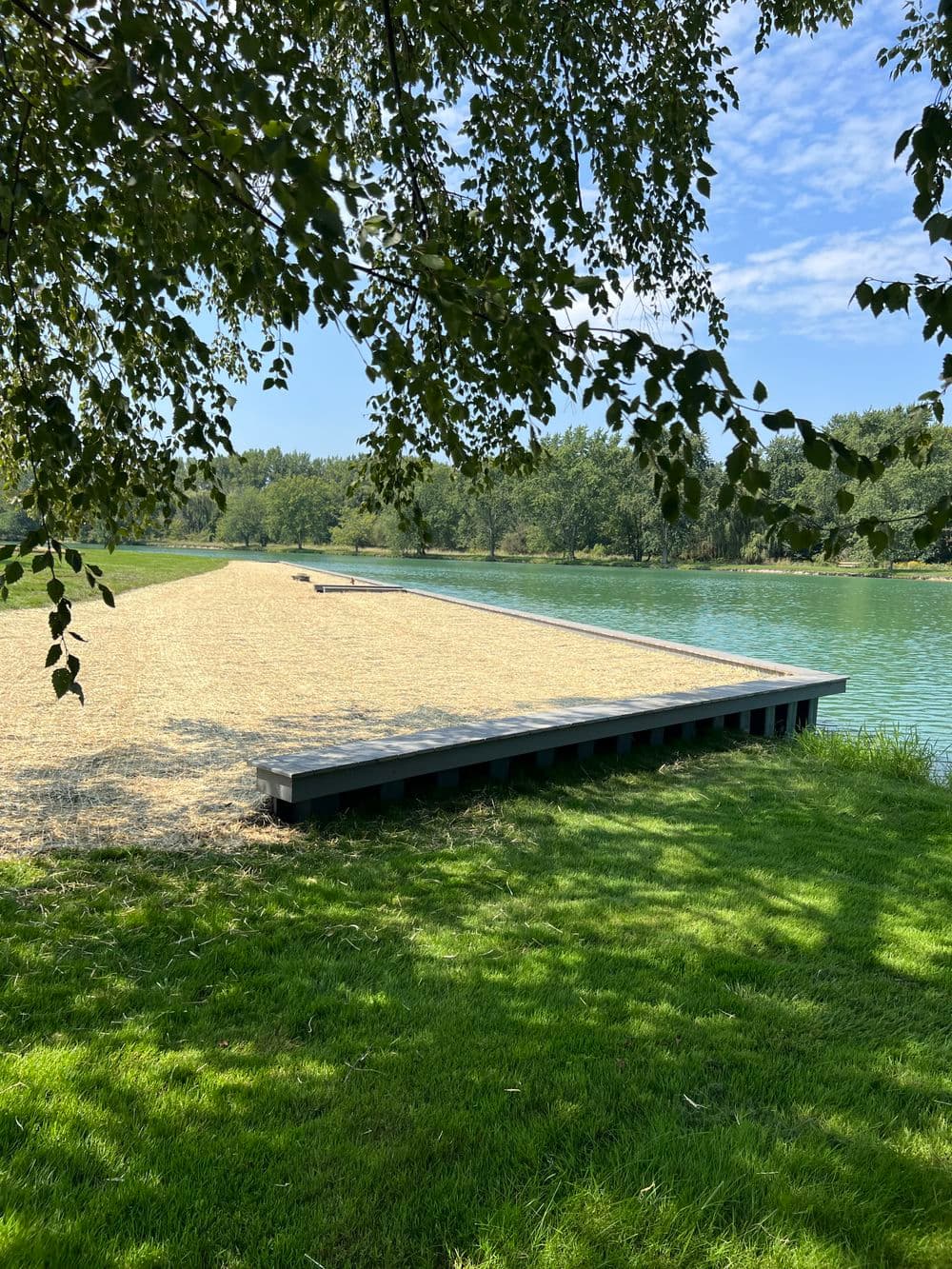 Dock by a serene lake, surrounded by green grass and trees under a clear blue sky.