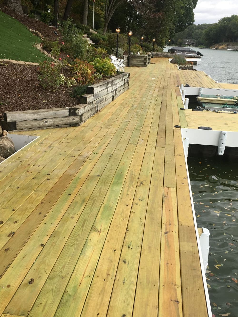 Wooden dock pathway with greenery and lampposts along the water's edge. Ideal for relaxation.