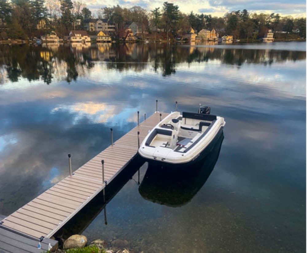 Boat docked at a wooden pier on a calm lake with charming houses in the background.